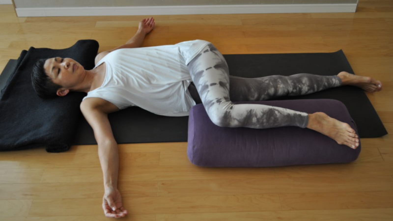 Young woman practicing Supported Supine Twist (Jathara Parivartanasana).