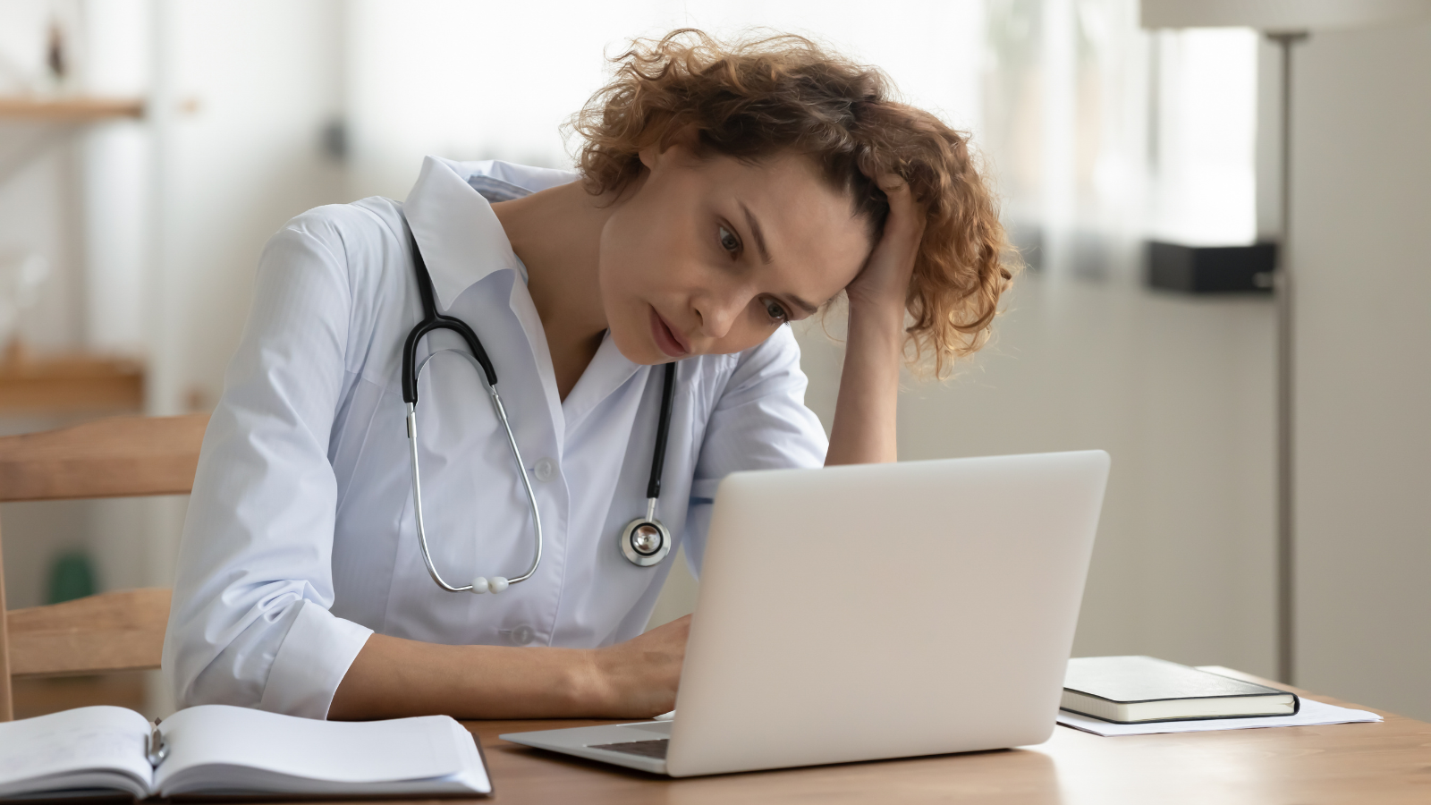 Stressed young female doctor looking at laptop reading bad news online worried of mistake at workplace.Title Text: Unhappy professional physician feeling tired and tense.