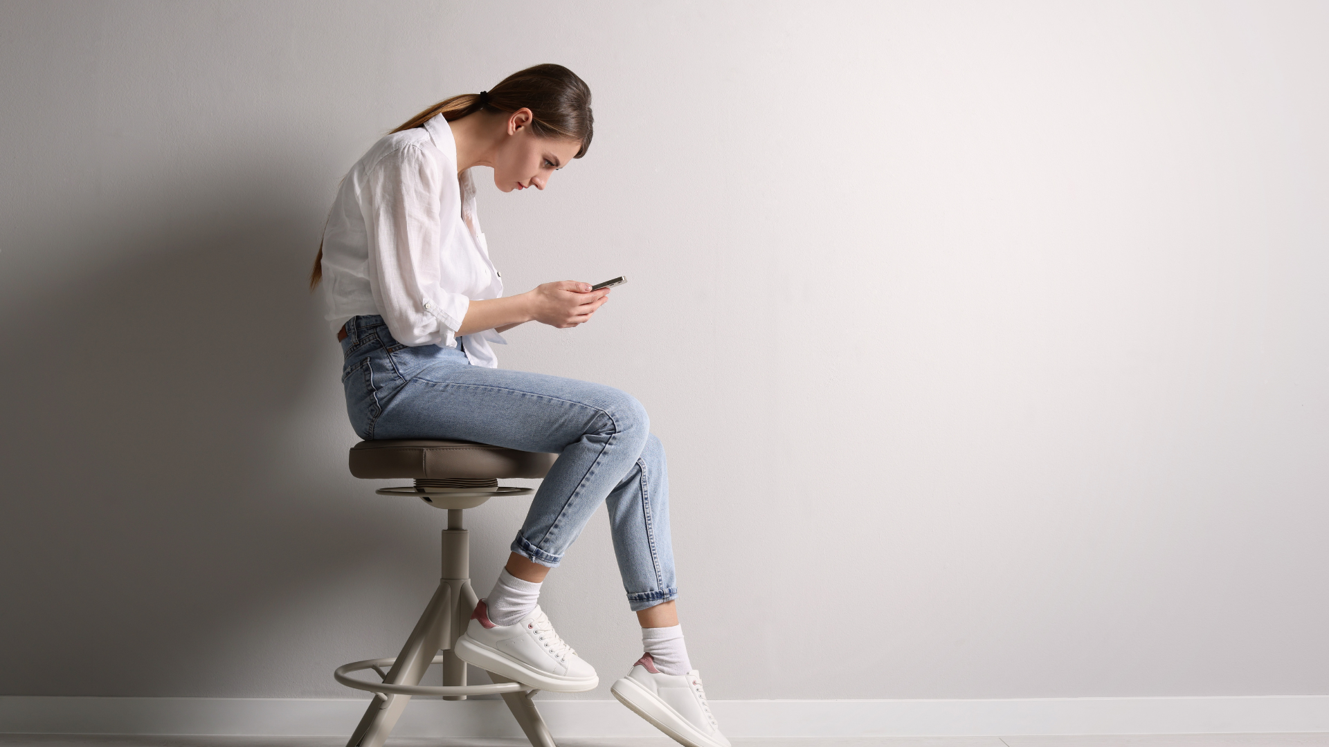 Woman with bad posture using smartphone while sitting on stool.