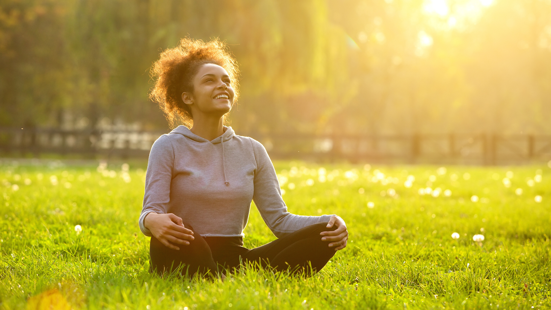 Young woman happily sitting outside in beautiful field.