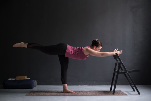 Woman practicing iyengar yoga warrior 3 with a chair