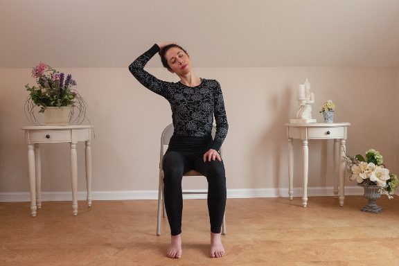 Woman seated in a chair stretching her neck yoga