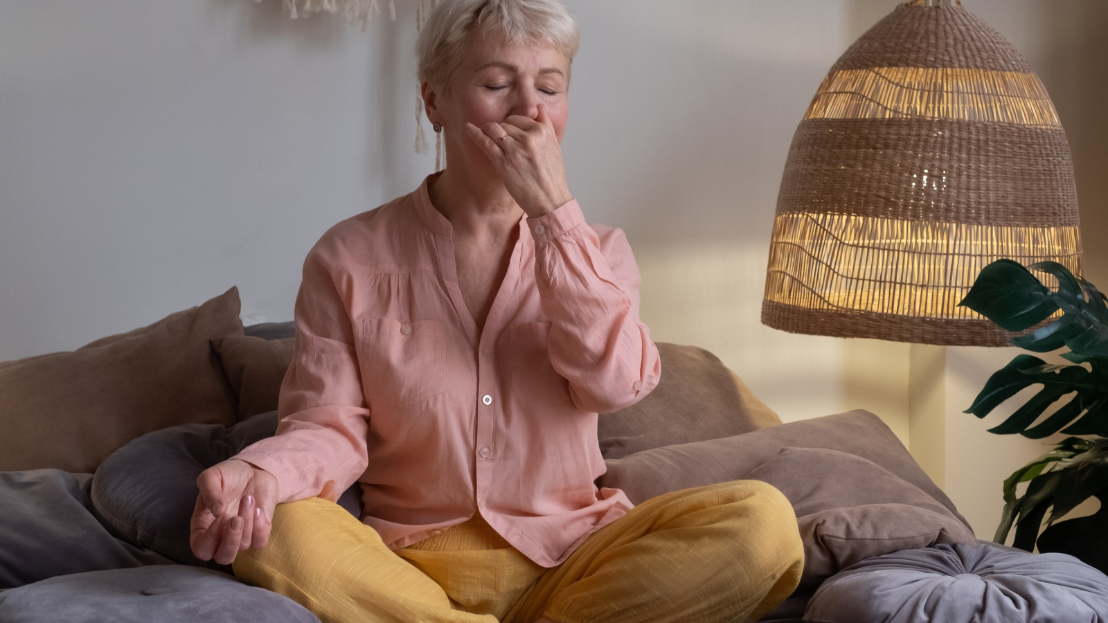 Senior woman practicing yoga at home making Alternate Nostril Breathing exercise (nadi shodhana pranayama pose)