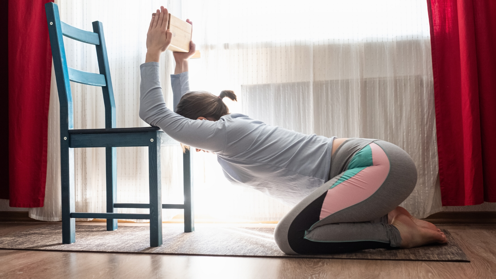 female yoga student practicing gentle yoga with a chair at home.