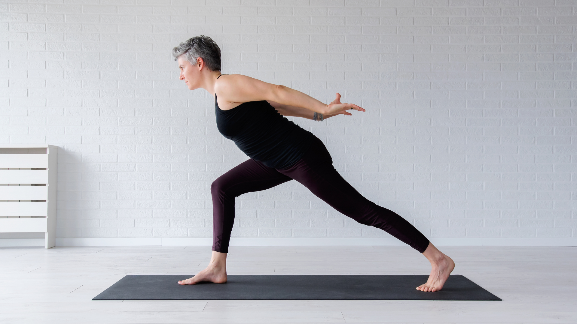 A senior woman practicing Virabhadrasana I (Warrior I Pose) to increase strength and flexibily.