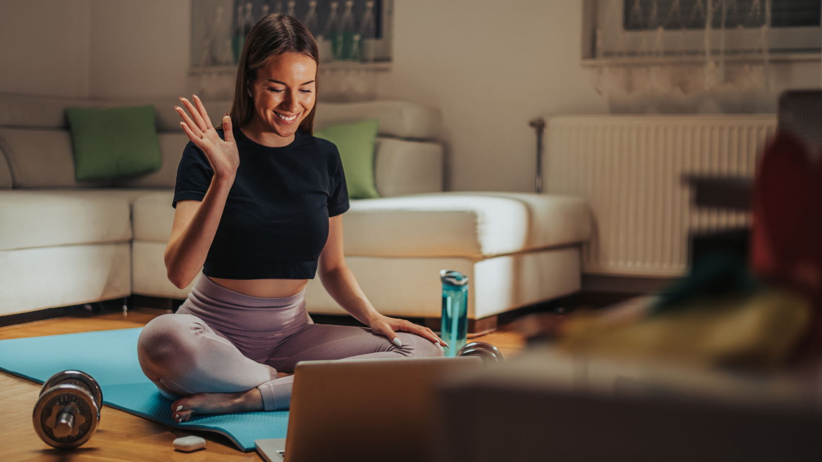 Young woman sitting in front of laptop in Sukhasana (Easy Pose), interacting with peers in online yoga teacher training.