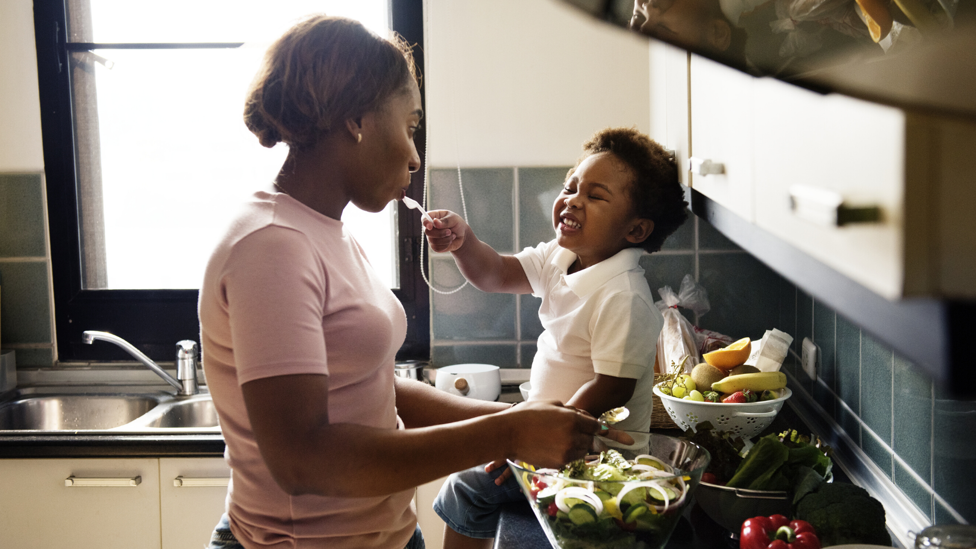 Little boy feeding his mother food while cooking.