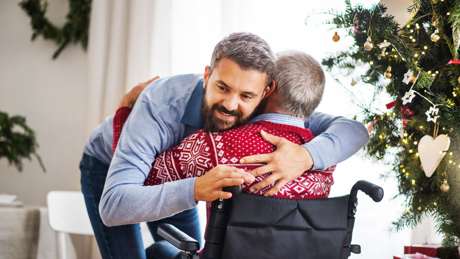 A hipster man hugging his disabled senior father in wheelchair at Christmas time