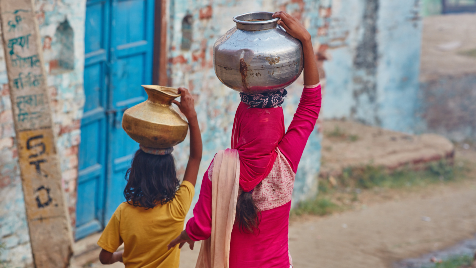 Two women with beautiful posture carrying jars on their head.