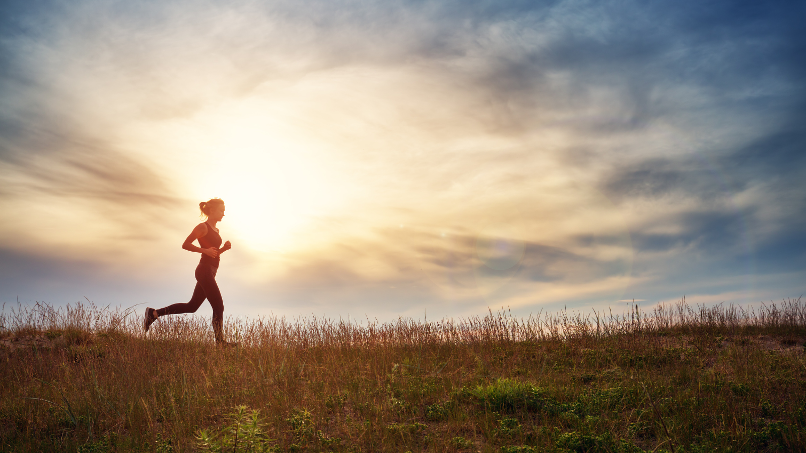 Young woman running on the field near seaside at sunset. Active person outdoors at the dusk in summer