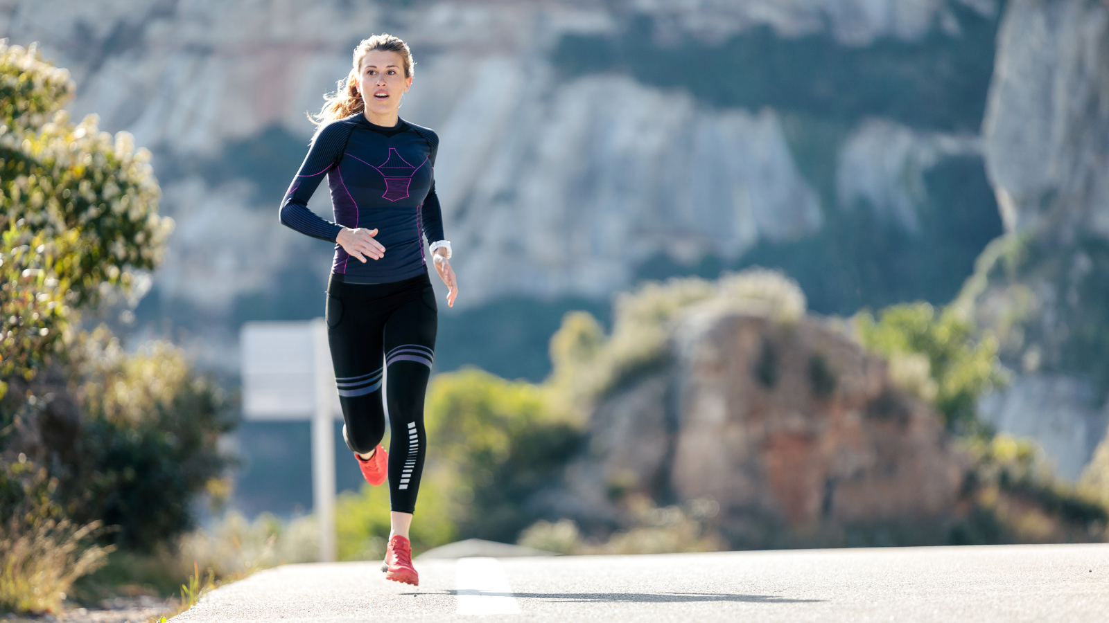 Sporty young woman running on mountain road in beautiful nature.