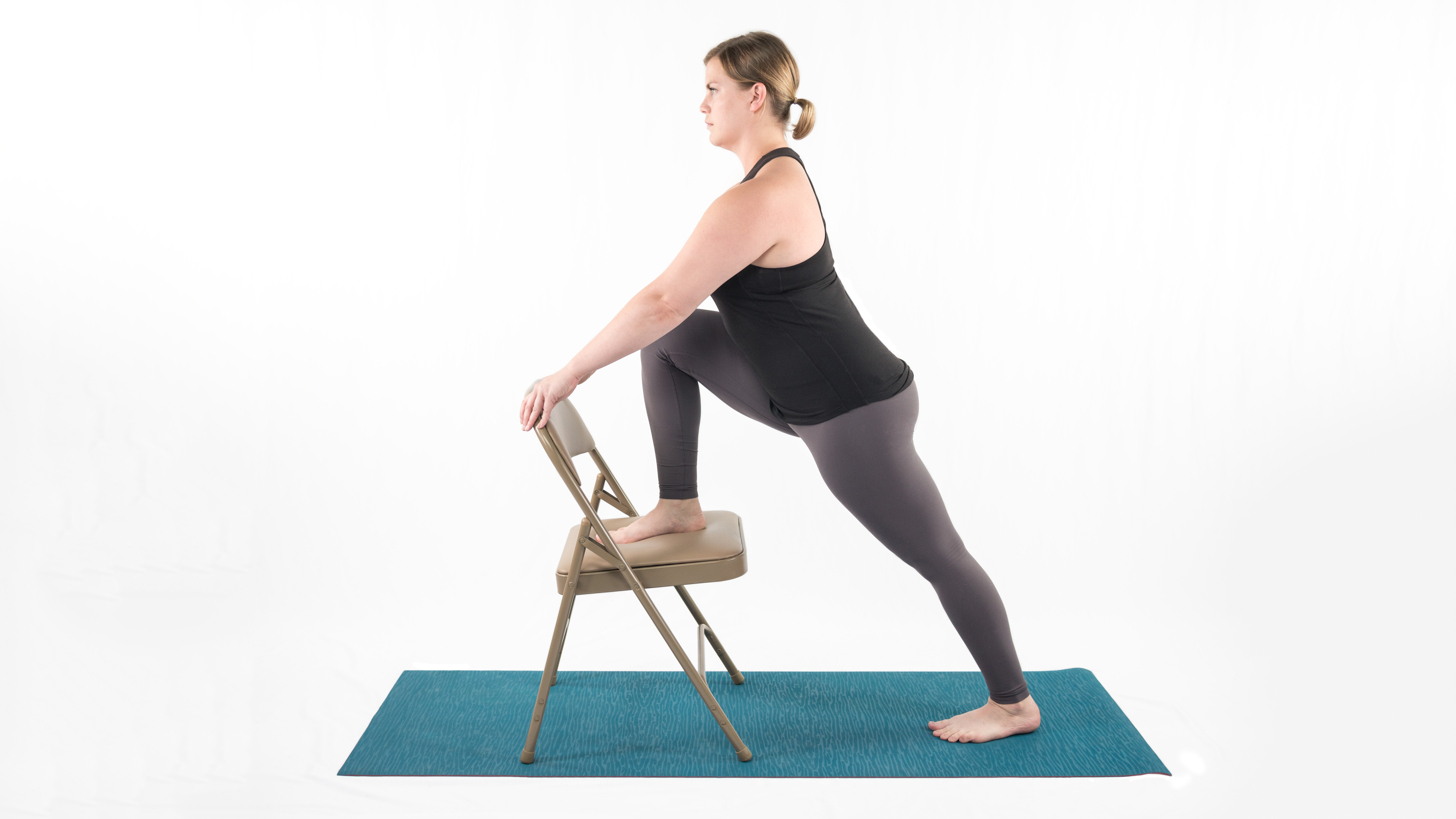 A woman in Lunge with Chair, which stretches the leg muscles in preparation for Warrior 2 yoga pose