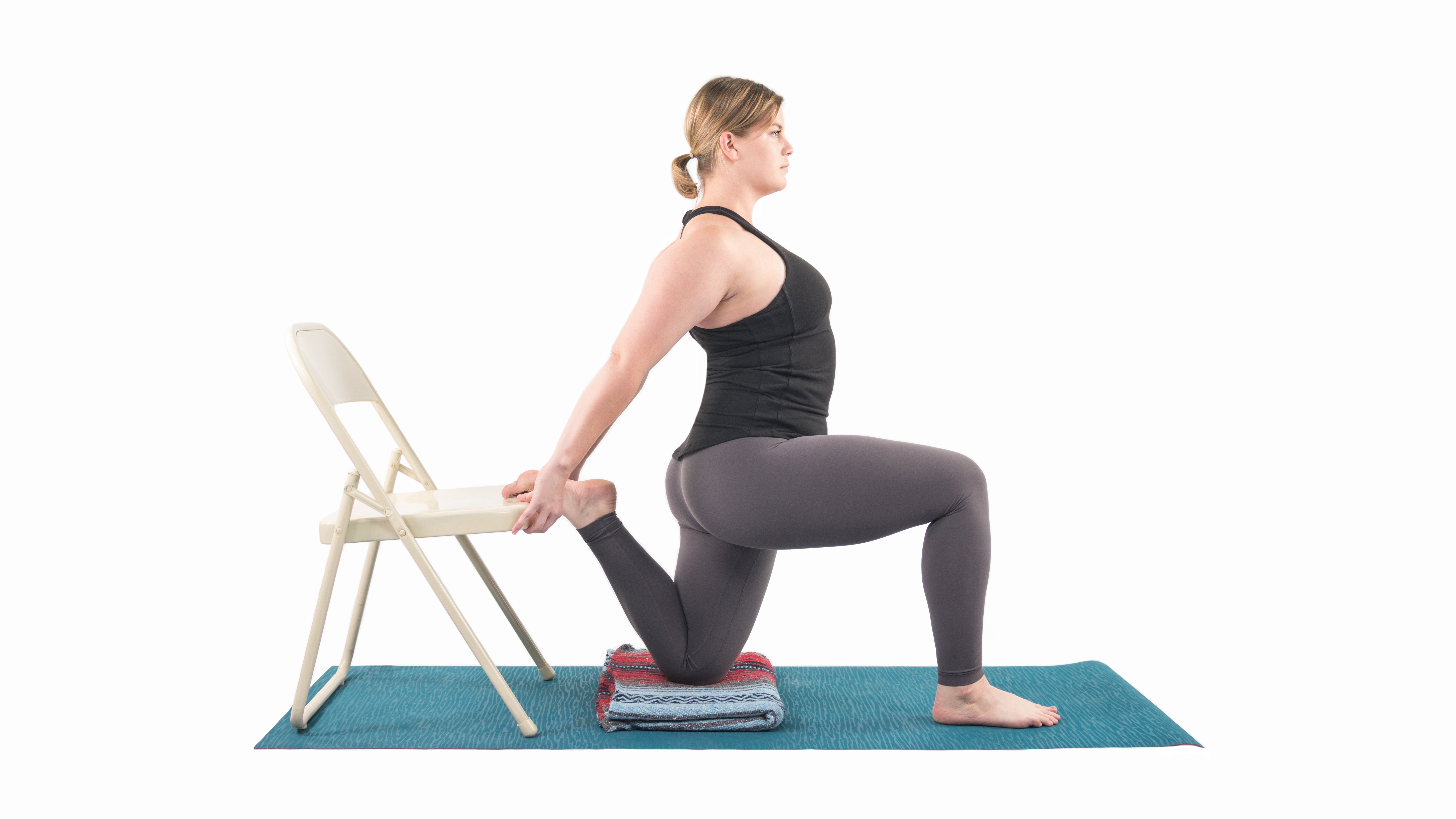 Woman performing a quad stretch with the support of a chair in preparation for the Dancer Pose