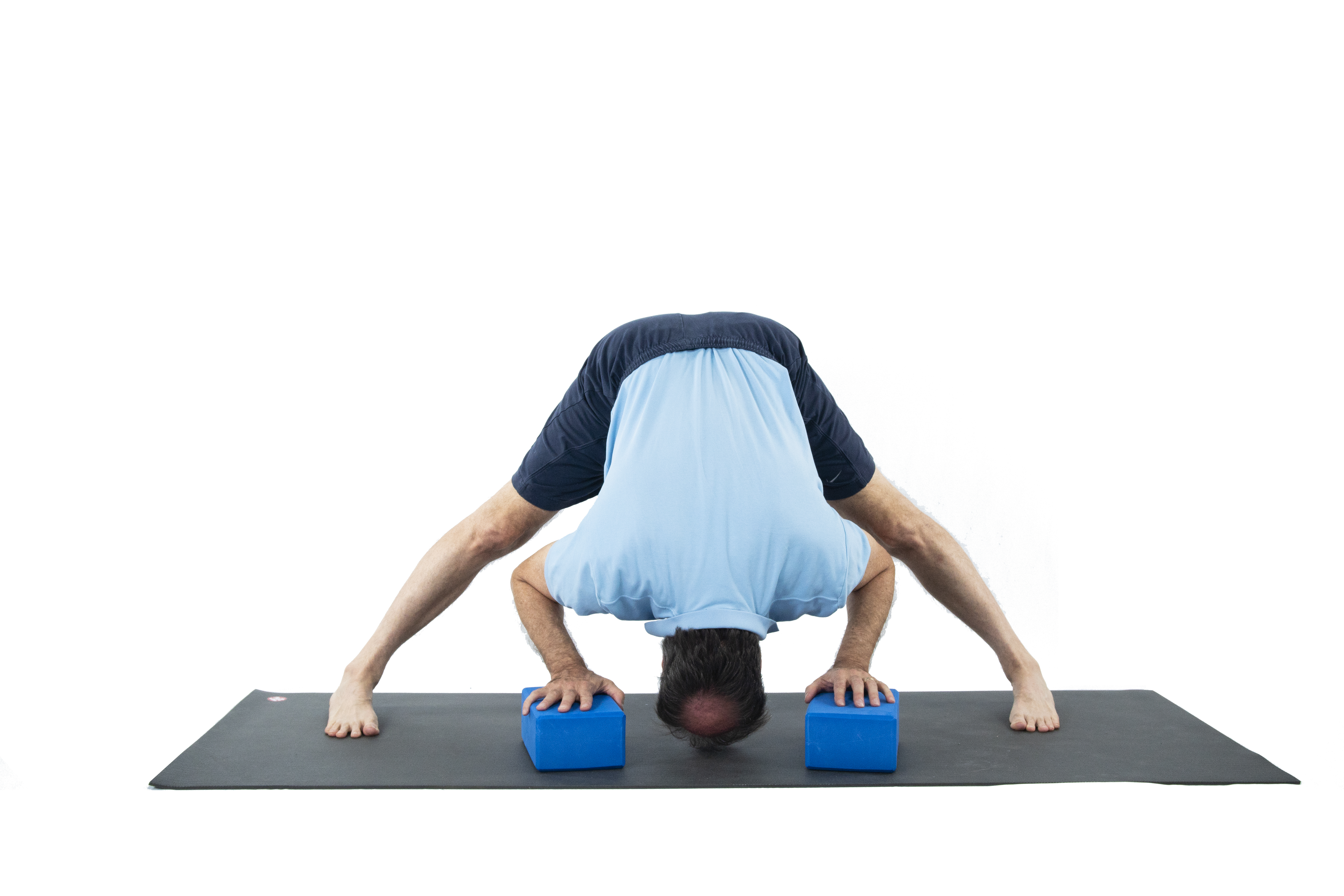 A man doing Wide-Legged Forward Fold (Prasarita Padottanasana) to prepare for the Warrior 2 yoga pose series