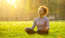 Happy young woman sitting outdoors in yoga's Easy Pose resting and enjoying nature.