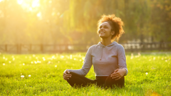 Happy young woman sitting outdoors in yoga's Easy Pose resting and enjoying nature.