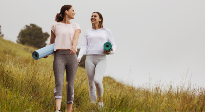 Smiling friends walking in the meadows with yoga mats. Concept of being in nature.