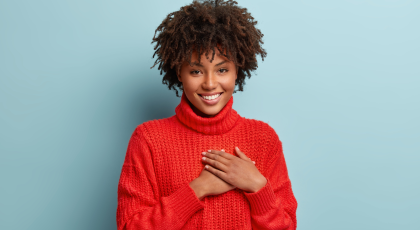 Photo of emotional female touching her heart with both palms, demonstrates thankful gesture.