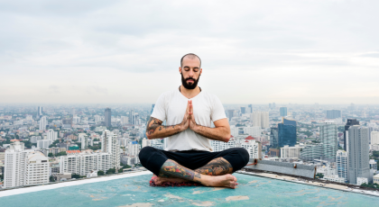 Man Practicing Yoga on a Rooftop with the world behind him.