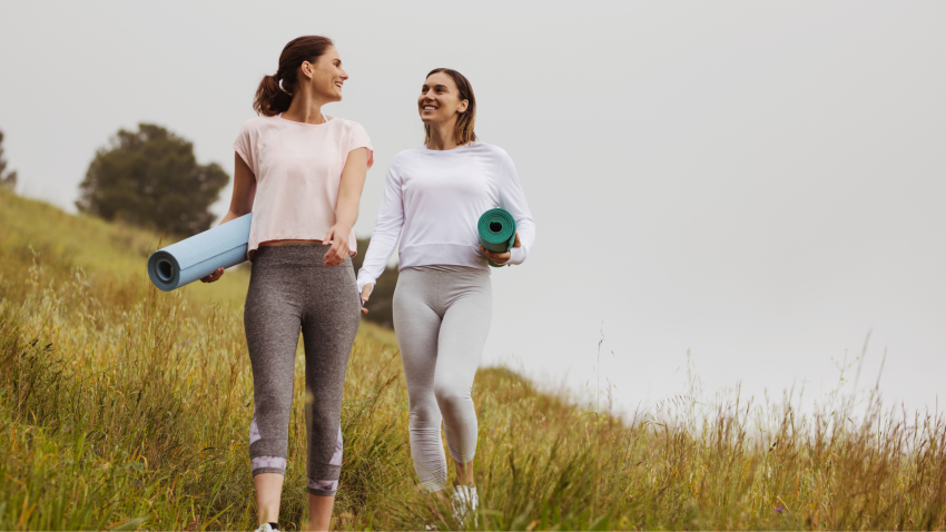 Smiling friends walking in the meadows with yoga mats. Concept of being in nature.