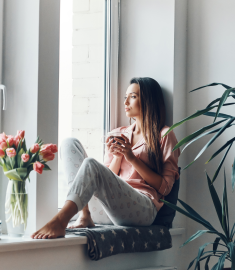 Thoughtful young woman in cozy pajamas looking through the window while resting at home