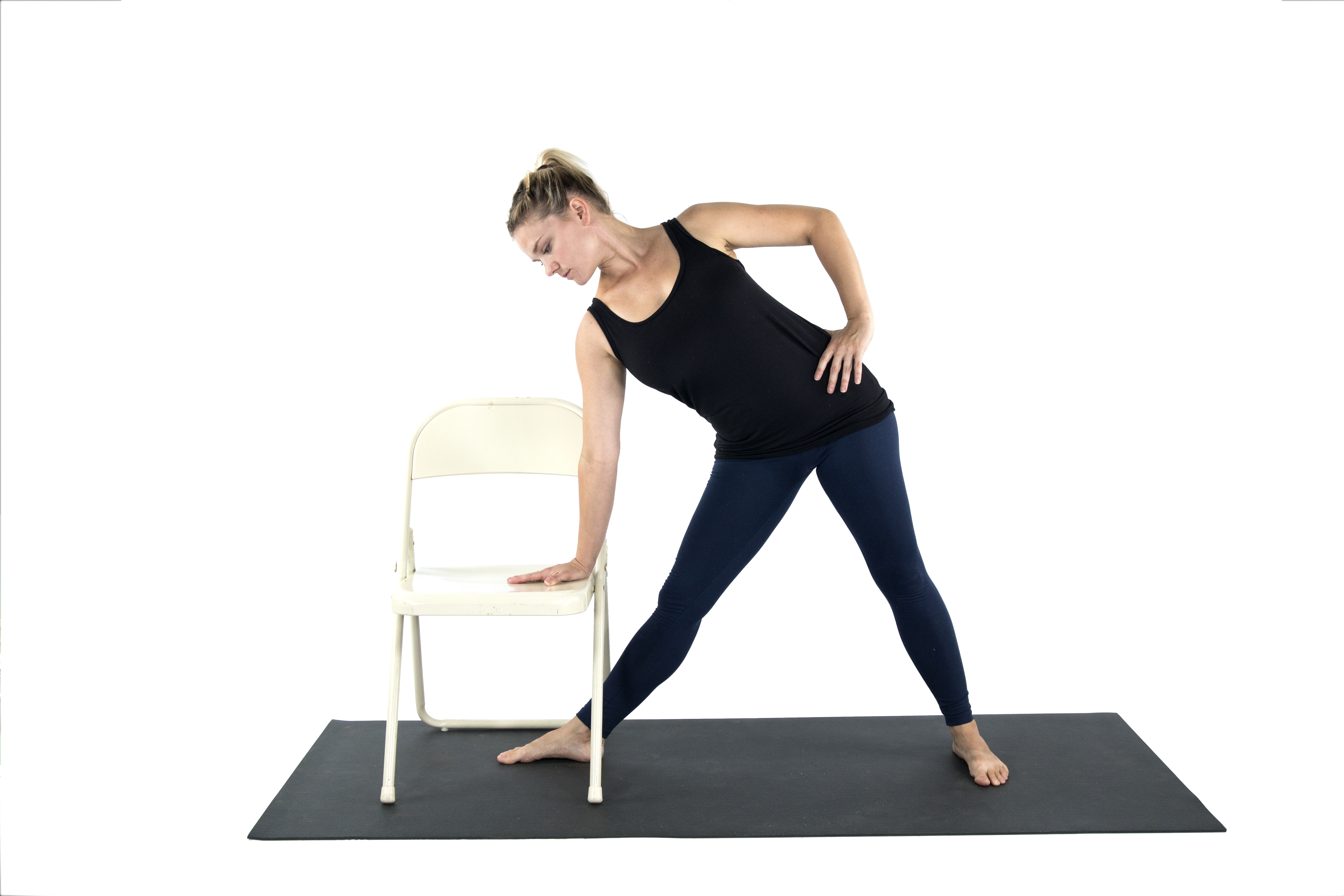 A woman doing a variation of Triangle Pose with the support of a chair in preparation for Warrior 2 yoga pose